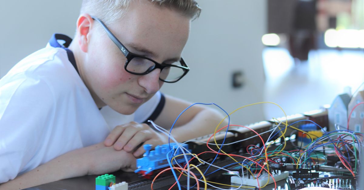 Boy engaged with electronic project involving toy train and wires indoors.
